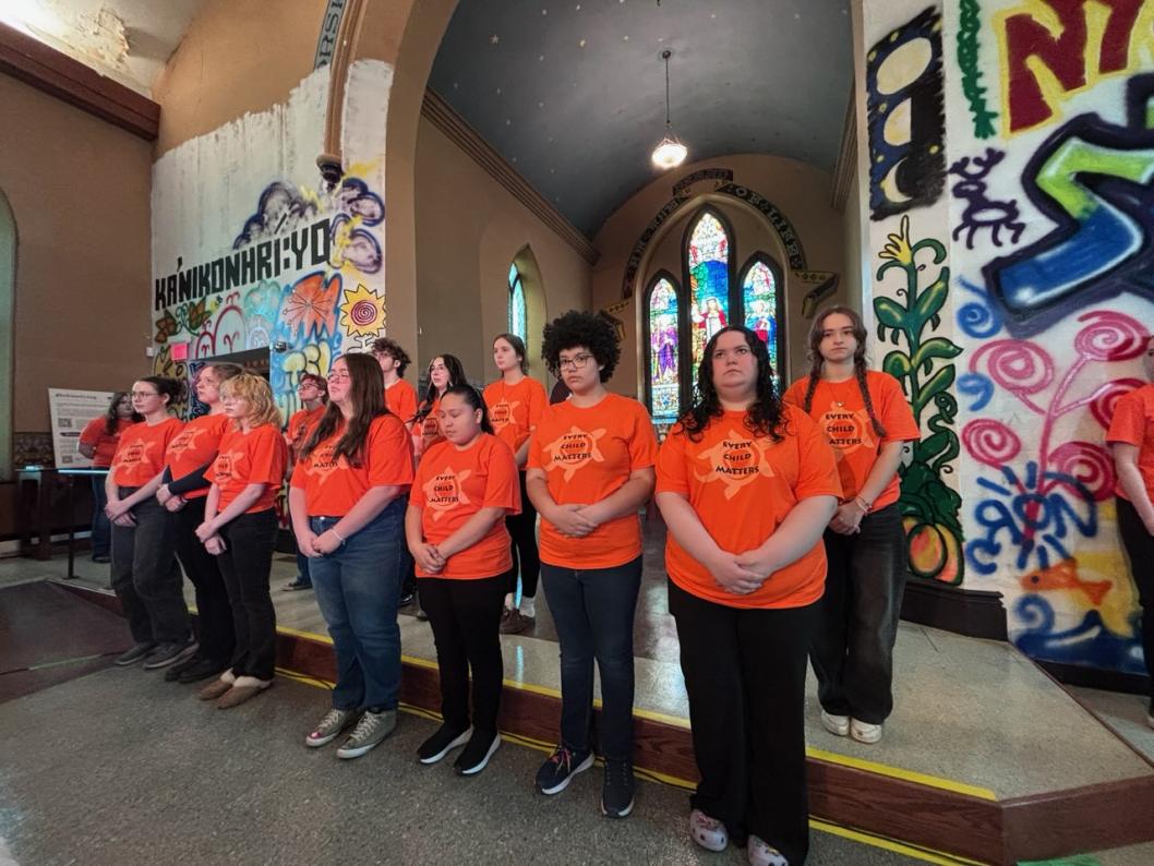 Students standing in two rows in front of graffiti and art work assembled to perform
