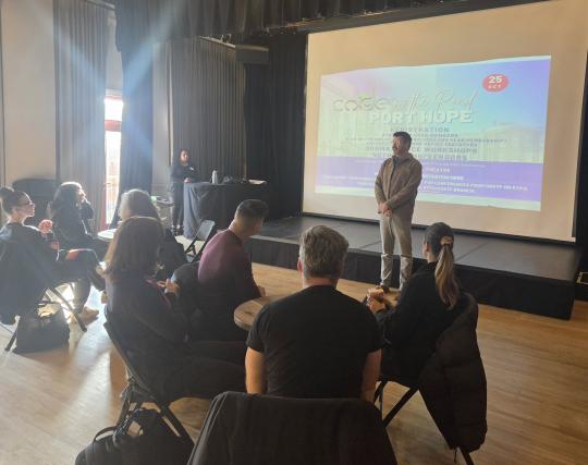 Rob Kempson standing in front of delegates at the CODE on the Road in Port Hope.  There is a screen that has the event information on it behind him